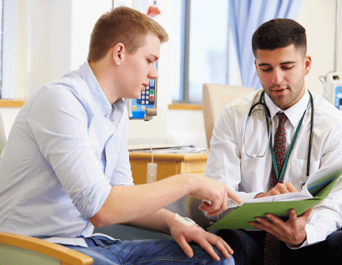 A doctor and a patient sit together as the doctor shows the patient information in a file. The patient has an IV in his arm.