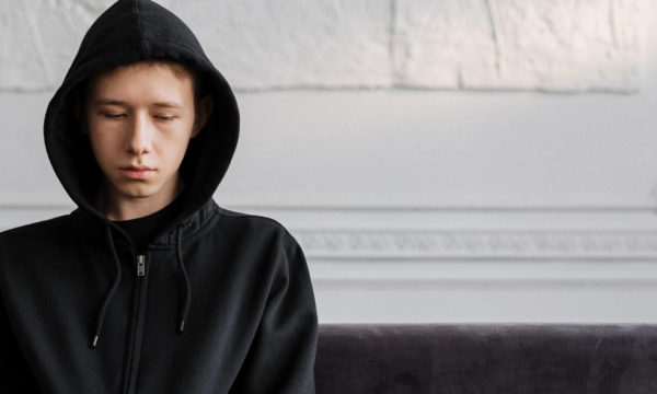 person wearing hooded jacket thinking deeply while sitting in a couch