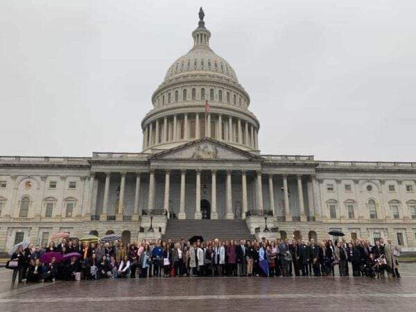 A large group of people stands in front of the United States Capitol building on a cloudy day.