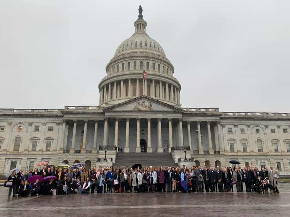 A large group of people stands in front of the United States Capitol building on a cloudy day.