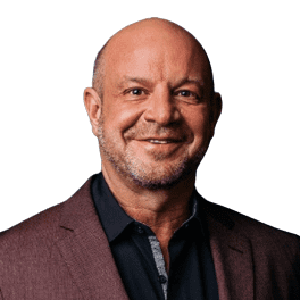 A middle-aged man with a bald head and trimmed beard, wearing a burgundy blazer over a dark shirt, smiling at the camera against a white background.