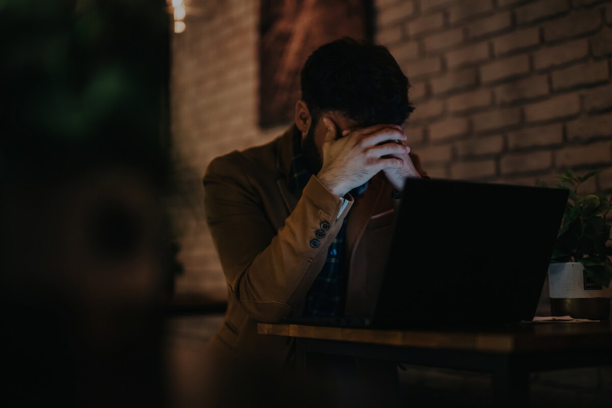 stressed businessman at desk with laptop in dimly lit office