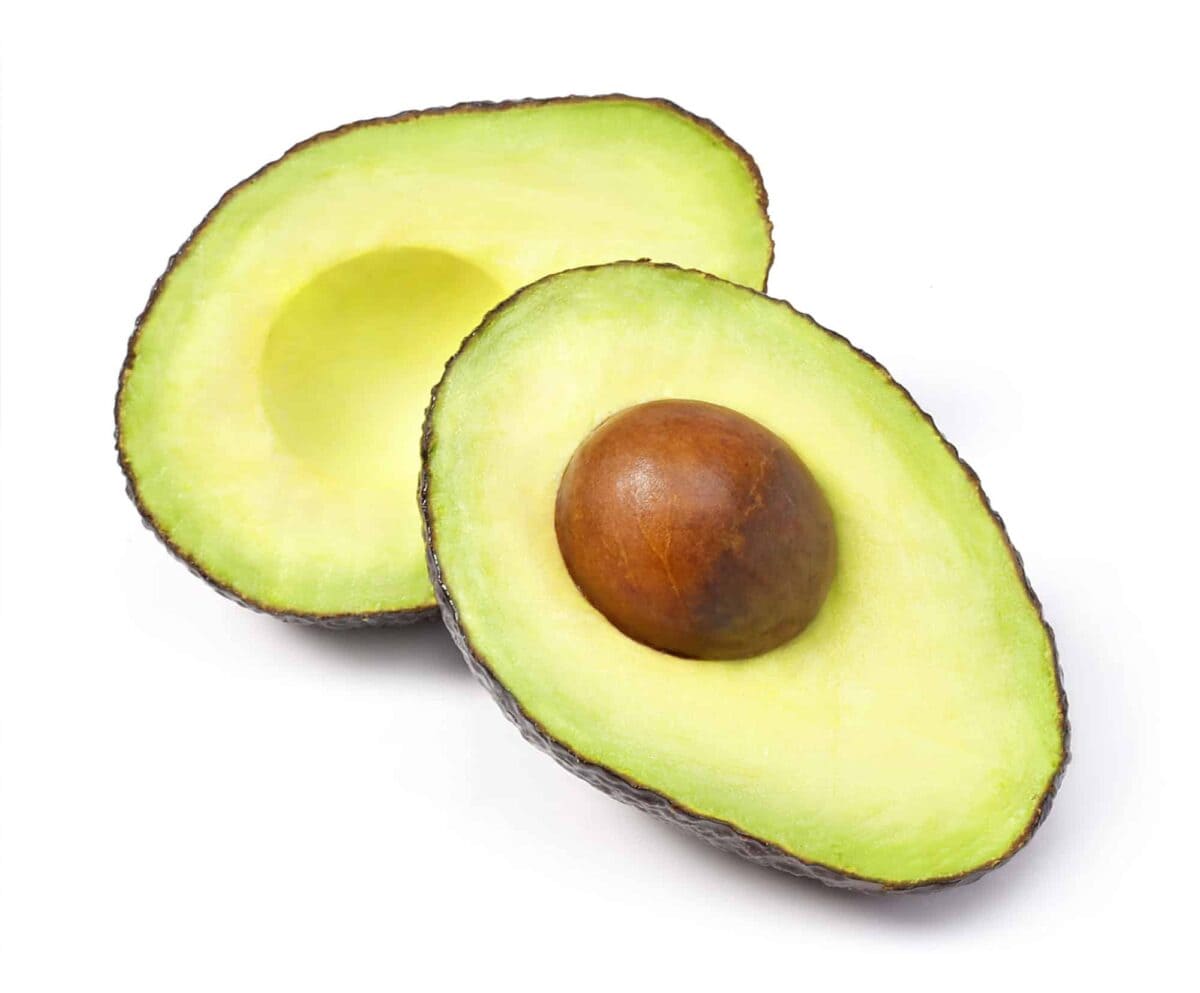Two avocado halves on a white background, one with the pit still inside and the other with the pit removed.