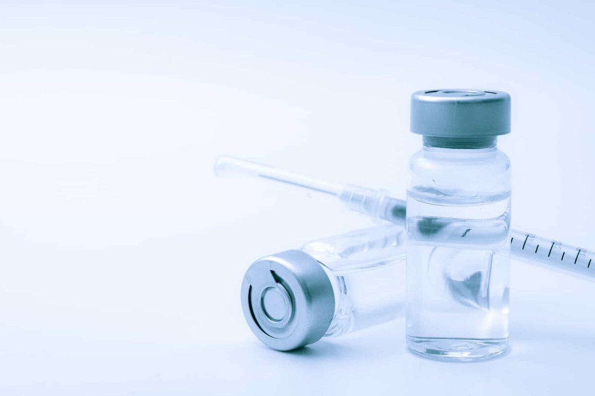 Two clear vials with liquid and a syringe are arranged on a white surface with a blue tint.