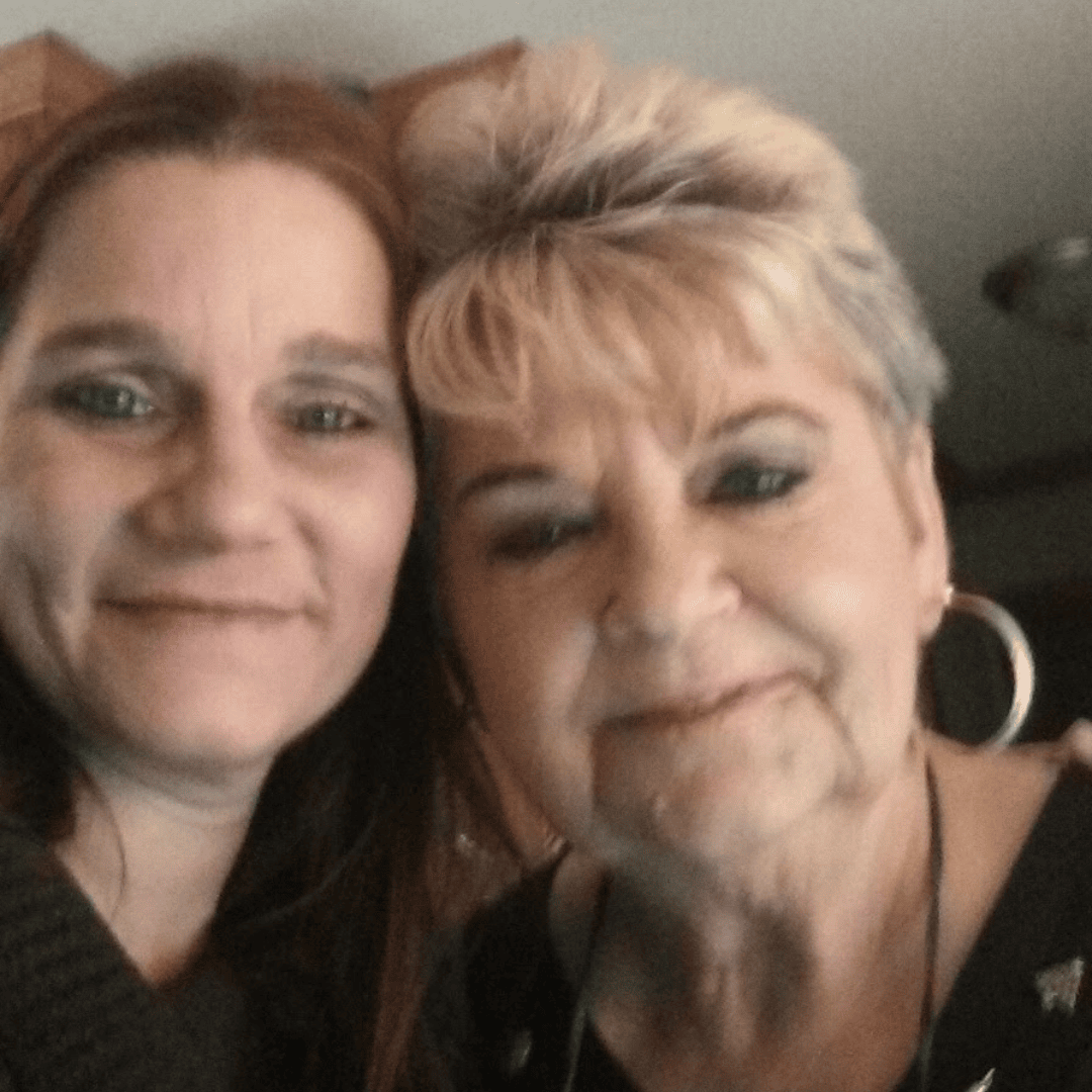 Two women are posing closely together for a selfie indoors, both smiling at the camera.