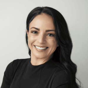 Woman with dark hair wearing a black shirt, smiling in front of a gray background.