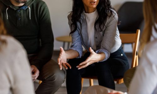 Cut out shot of anxious woman sitting in circle and talking about her mental health struggles with her peers during a group therapy session.