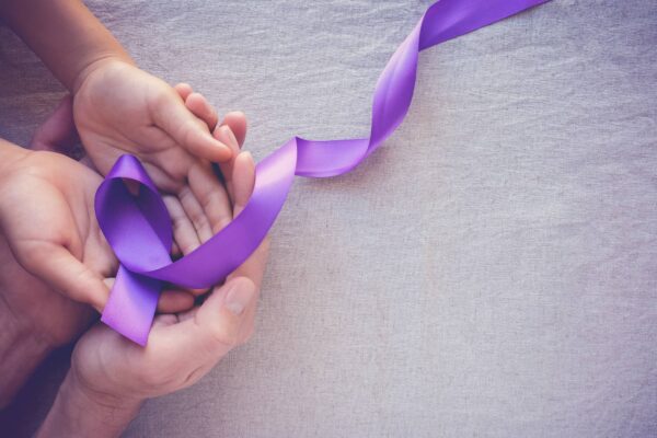 Adult hands holding a child's hands, both cupping a purple awareness ribbon on a light textured surface.