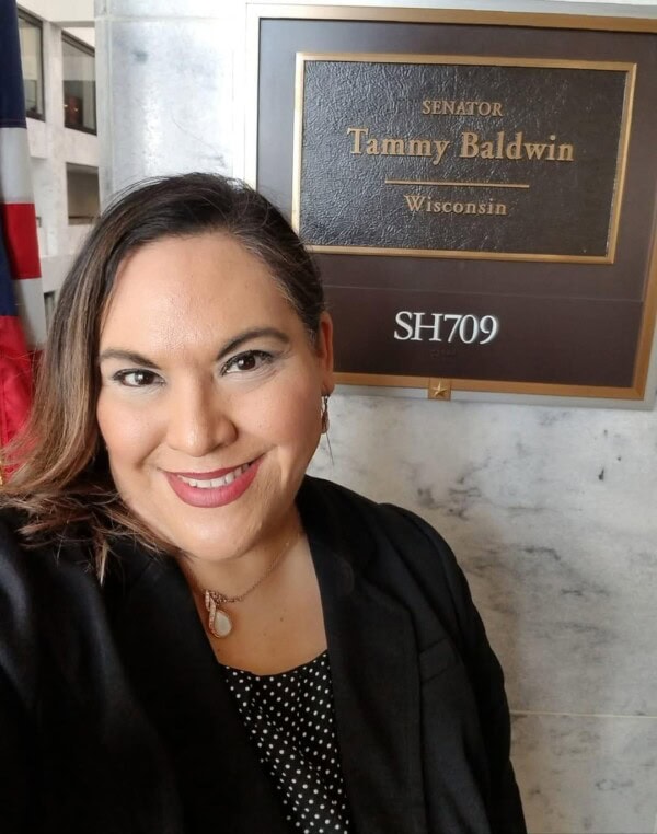 A woman smiles for a selfie in front of an office sign that reads 