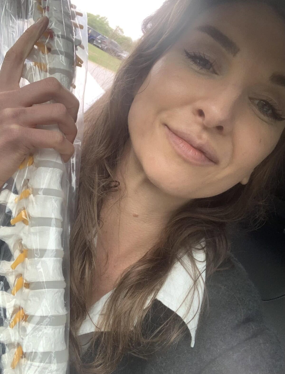 A woman holds a model of a human spine, smiling at the camera.
