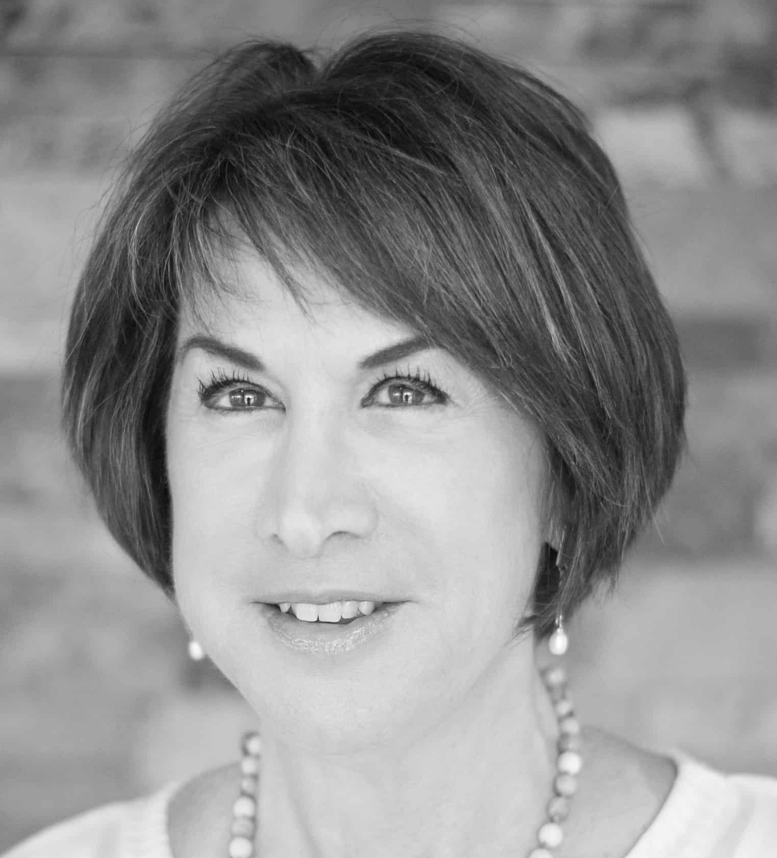 Black and white portrait of a middle-aged woman with short hair, wearing a necklace, smiling softly, and looking at the camera.
