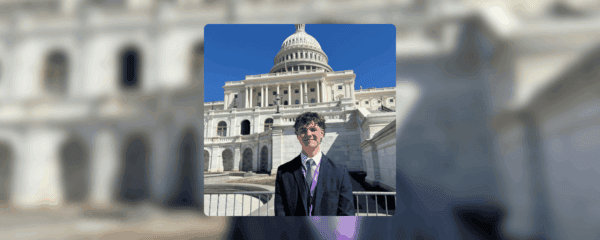 A person in a suit stands in front of the U.S. Capitol building on a sunny day.