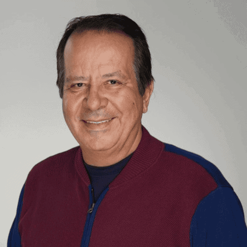 A middle-aged man with short dark hair smiles, wearing a maroon jacket over a navy shirt, against a plain light gray background.
