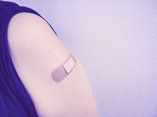 A close-up of an upper arm with a bandage applied, against a plain background.