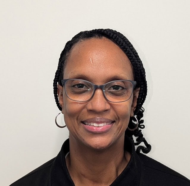 A woman with glasses and braided hair is smiling at the camera against a plain white background.