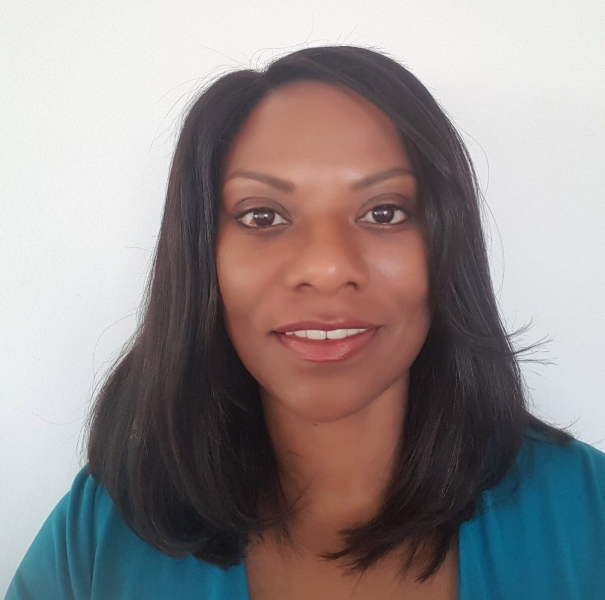 A woman with straight, shoulder-length dark hair and brown eyes is facing the camera and smiling slightly. She is wearing a teal top and is positioned against a plain white background.