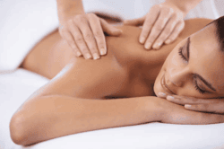 A person receives a back massage while lying on a white towel, with eyes closed and a relaxed facial expression.