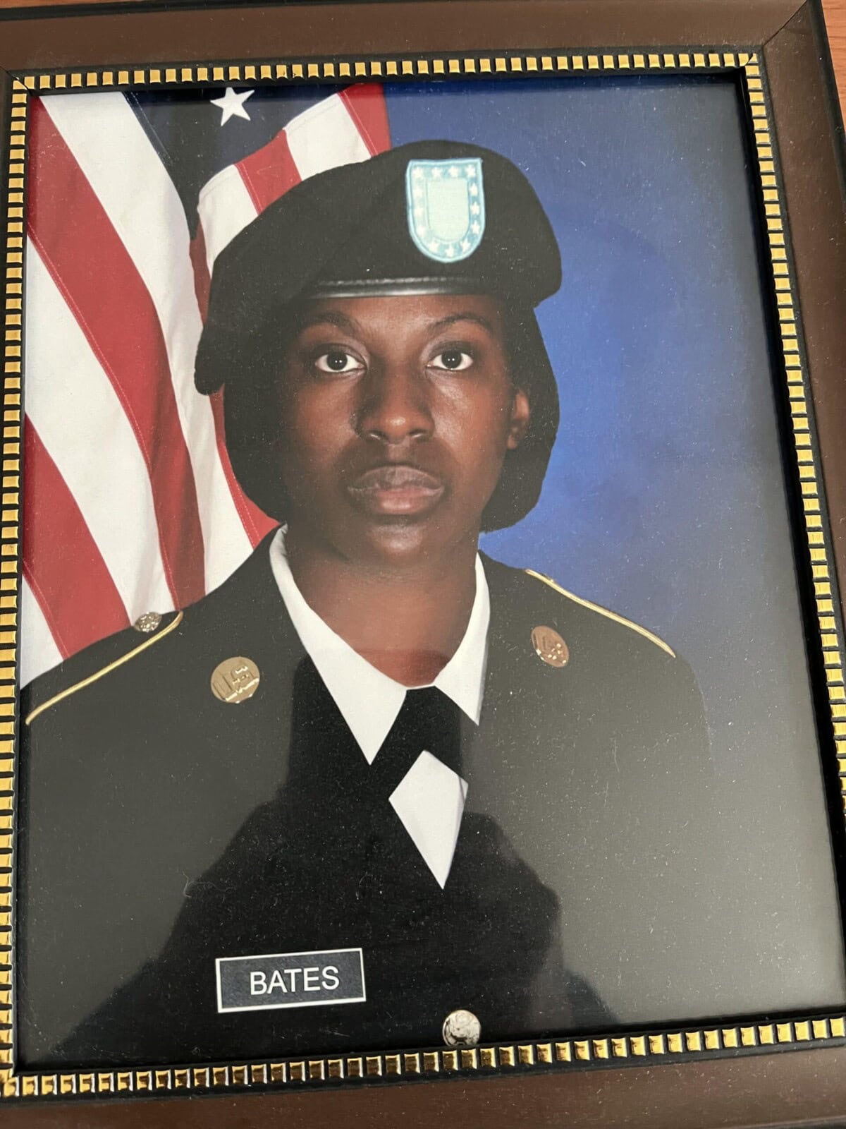 A framed portrait of a person in military uniform with a name tag reading "Bates," posing in front of an American flag.
