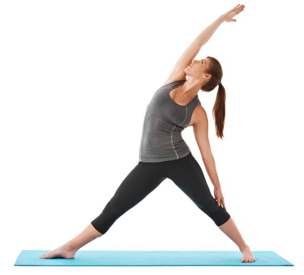 A woman on a blue yoga mat performs a standing side stretch, with one arm reaching up and the other hand resting on her leg.